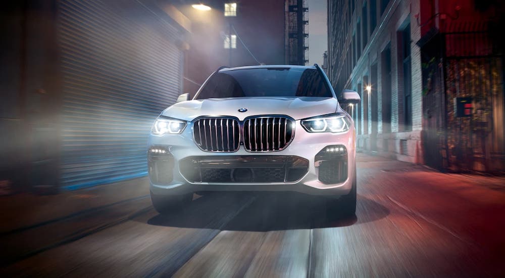 A white 2020 BMW X5 is shown from the front driving through a Cincinnati alley at night.