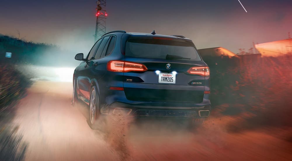 A blue 2020 BMW X5 is shown from the rear, driving on a dirt road at night.