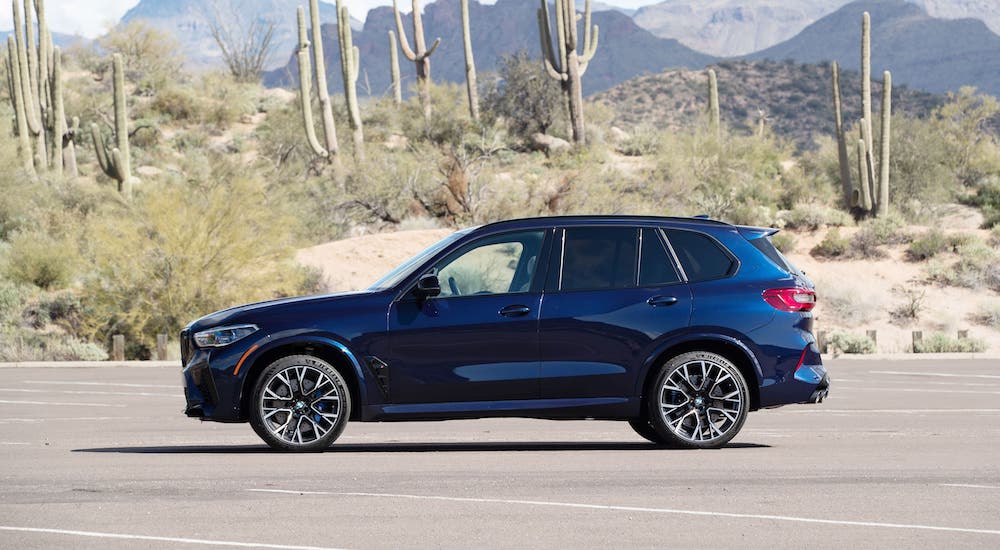 A blue 2020 BMW X5 M is shown from the side in a desert in front of cactus.