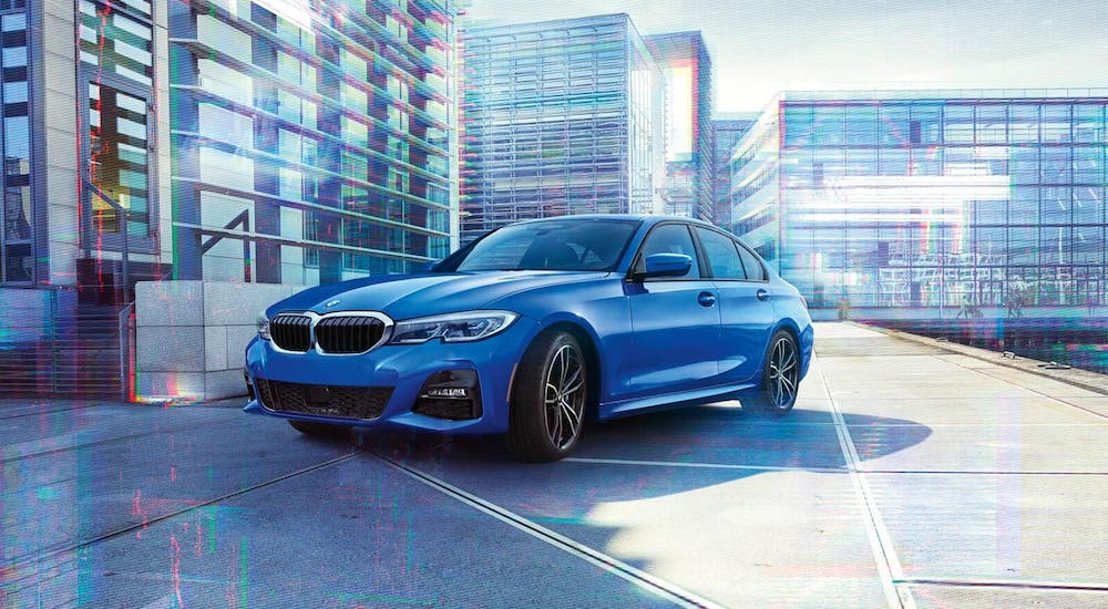 A blue 2020 BMW 3Series 330i us parked in front of glass buildings.