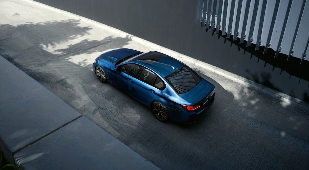 A blue 2021 BMW 5 Series is shown from a high angle driving in a concrete alleyway.