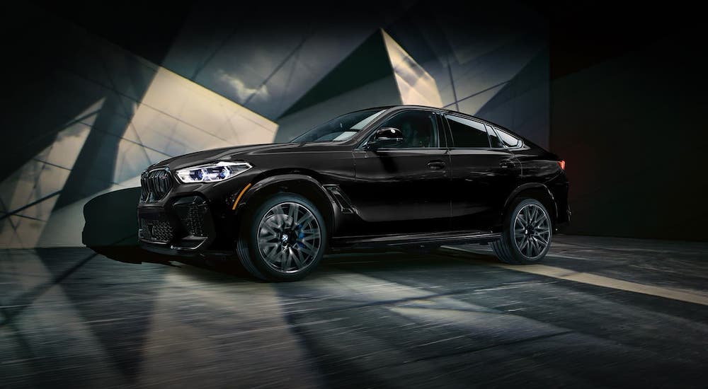 A black 2021 BMW X6 M series is driving in front of geometric shapes.