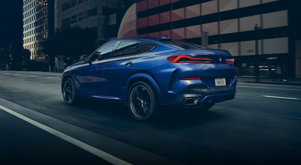 A blue 2022 BMW X6 is shown from a rear angle driving in the city.