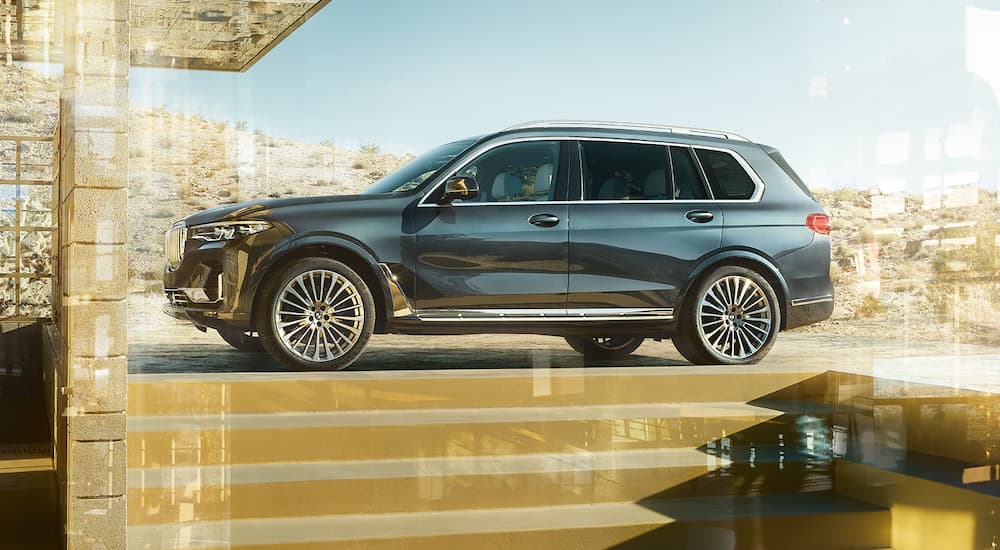 A grey 2022 BMW X7 SAV is shown from the side parked outside of a modern home.