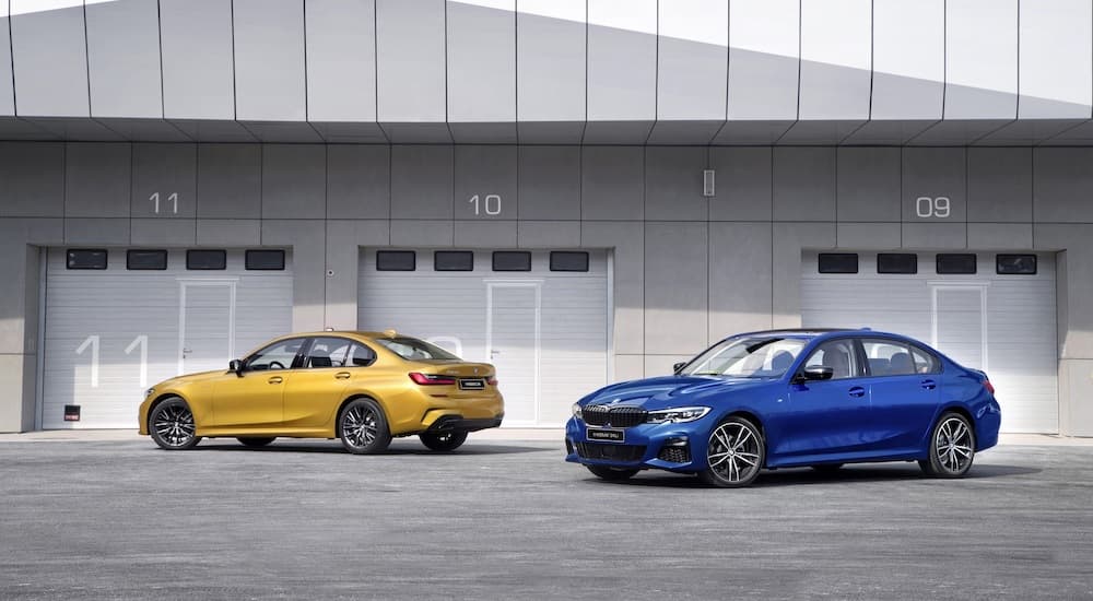 A yellow and a blue 2022 BMW 3 Series are shown parked in front of a large garage.