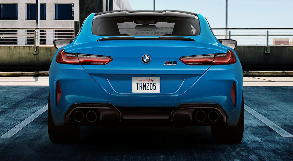 A blue 2022 BMW M8 Competition Coupe is shown from the rear in a parking spot.