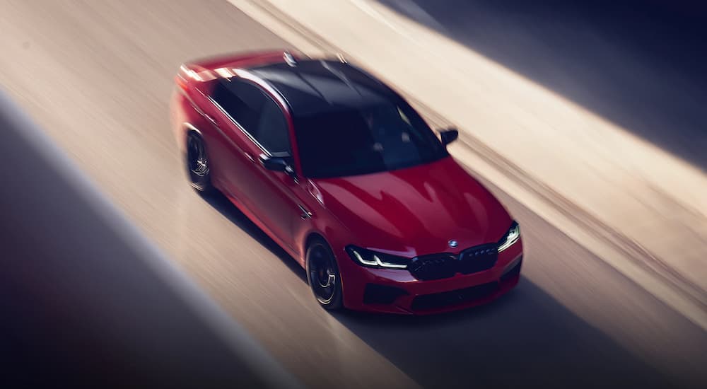 A red 2023 BMW M5 Sedan is shown driving on a city highway.