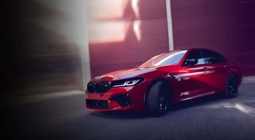 A red 2023 BMW M5 is shown driving on a city street.