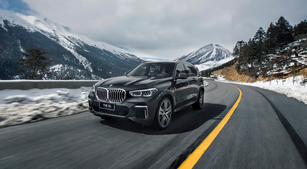 A black 2023 BMW X5 for sale is shown driving on a mountain road.