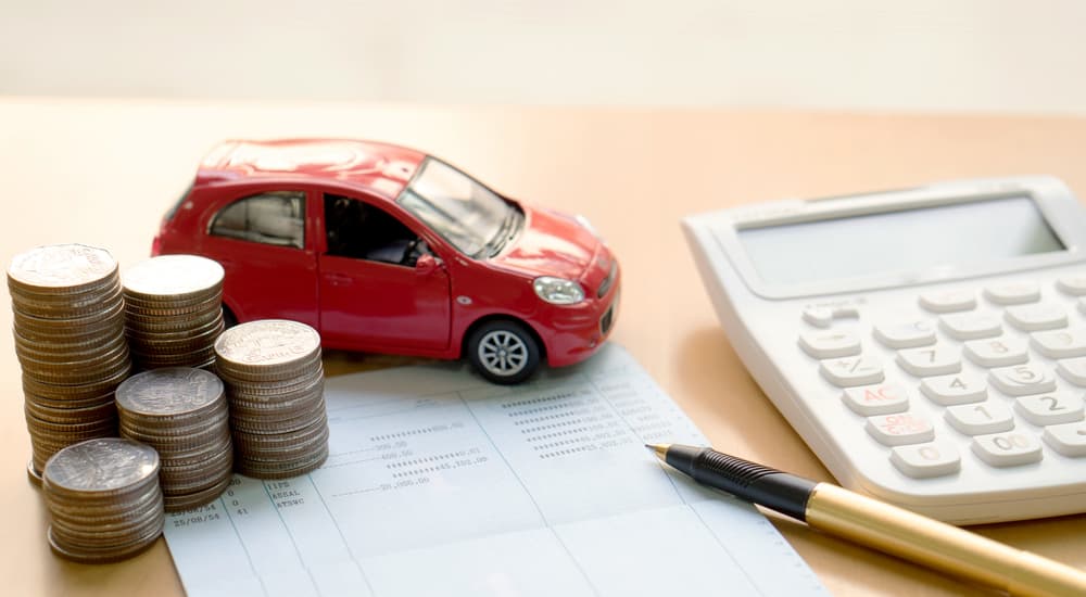 A red toy car is shown next to a stack of coins and calculator.